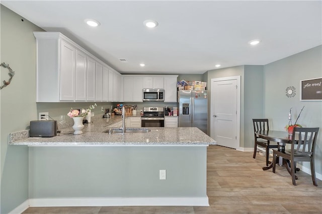 kitchen with kitchen peninsula, appliances with stainless steel finishes, light wood-type flooring, sink, and white cabinets