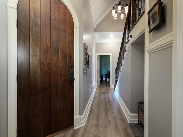 corridor with a chandelier, hardwood / wood-style floors, vaulted ceiling, and crown molding