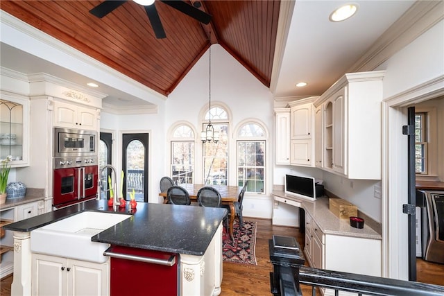 kitchen featuring dark wood-type flooring, vaulted ceiling with beams, an island with sink, a healthy amount of sunlight, and stainless steel appliances