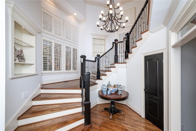 stairway with hardwood / wood-style flooring, a notable chandelier, ornamental molding, and a towering ceiling