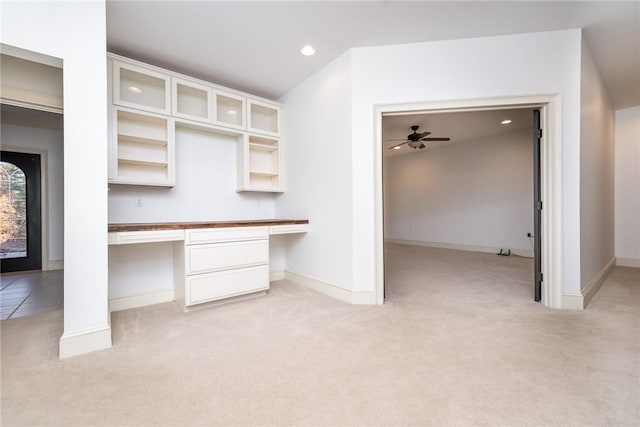 unfurnished office with light carpet, ceiling fan, and built in desk