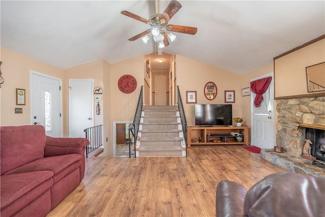 living room featuring a fireplace, light wood-type flooring, vaulted ceiling, and ceiling fan