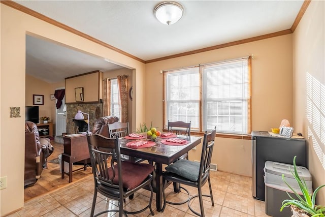 dining room featuring light hardwood / wood-style flooring, a stone fireplace, and crown molding