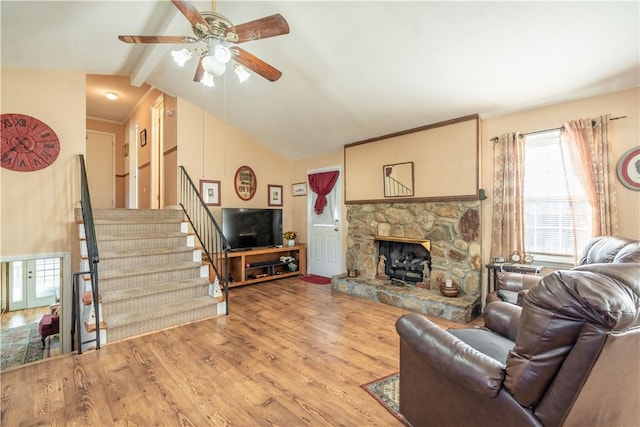 living room with vaulted ceiling with beams, light hardwood / wood-style floors, a stone fireplace, and ceiling fan