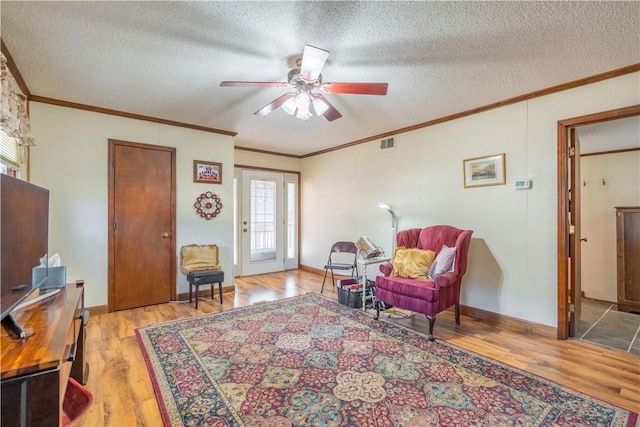 living area with a textured ceiling, light hardwood / wood-style floors, ceiling fan, and ornamental molding