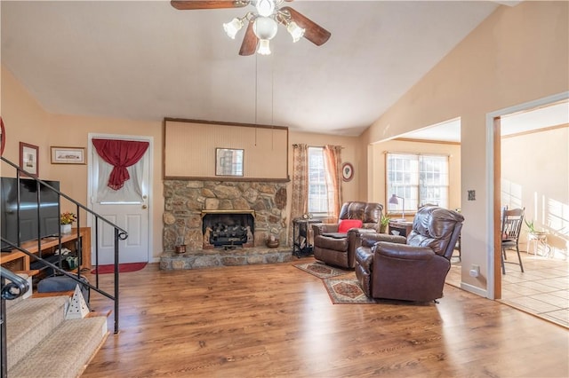 living room with wood-type flooring, high vaulted ceiling, a stone fireplace, and ceiling fan