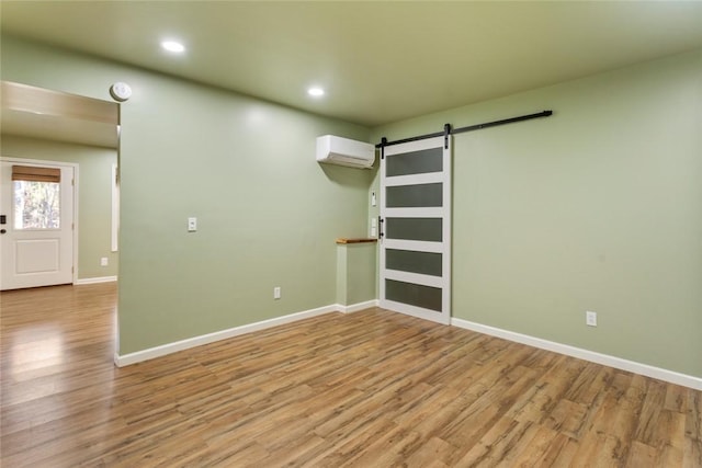 empty room with light hardwood / wood-style floors, a barn door, and an AC wall unit