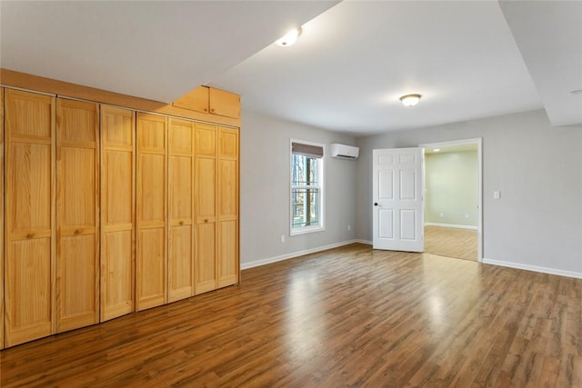 unfurnished bedroom featuring a wall mounted air conditioner, wood-type flooring, and a closet