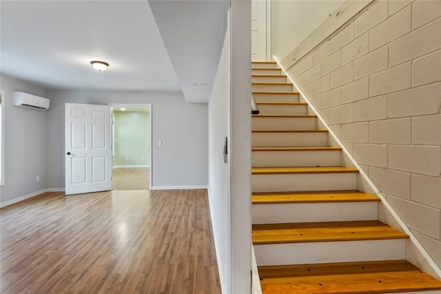 staircase with a wall mounted AC and wood-type flooring