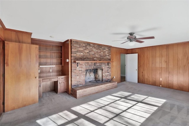 unfurnished living room featuring light carpet, ceiling fan, crown molding, wooden walls, and a fireplace