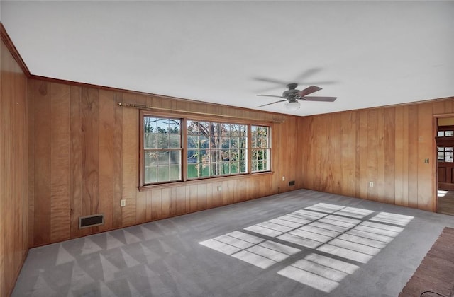 spare room with ceiling fan, crown molding, light carpet, and wooden walls