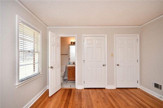 unfurnished bedroom featuring light wood-type flooring, connected bathroom, and multiple windows