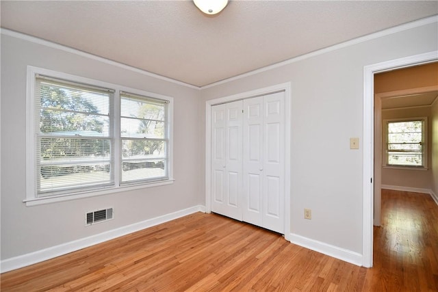 unfurnished bedroom with a closet, light wood-type flooring, crown molding, and multiple windows