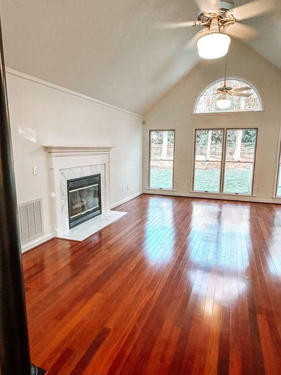 unfurnished living room featuring a premium fireplace, ceiling fan, wood-type flooring, and vaulted ceiling