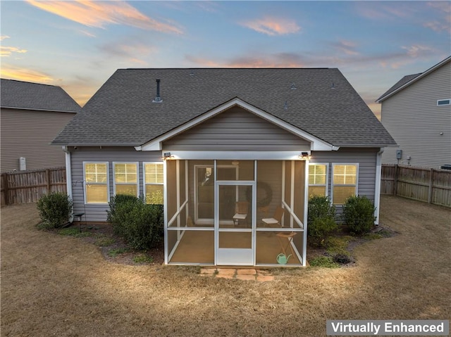 back house at dusk with a sunroom and a yard