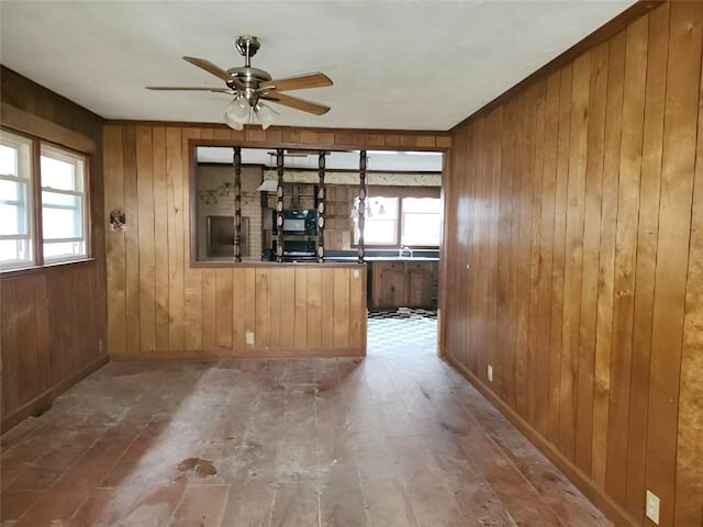 unfurnished living room featuring plenty of natural light, wood walls, and ceiling fan