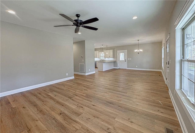 unfurnished living room with ceiling fan with notable chandelier and light hardwood / wood-style floors