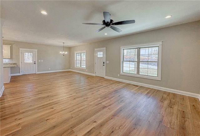 unfurnished living room with ceiling fan with notable chandelier, light hardwood / wood-style floors, and a wealth of natural light