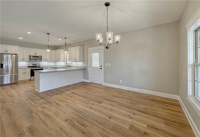 kitchen with kitchen peninsula, light wood-type flooring, stainless steel appliances, decorative light fixtures, and white cabinets