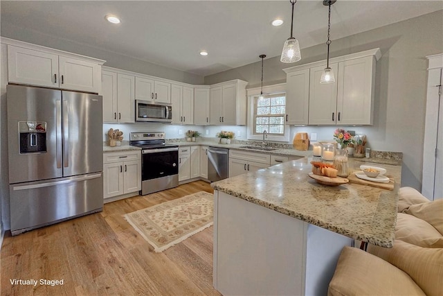 kitchen featuring a breakfast bar, stainless steel appliances, white cabinets, light hardwood / wood-style floors, and hanging light fixtures