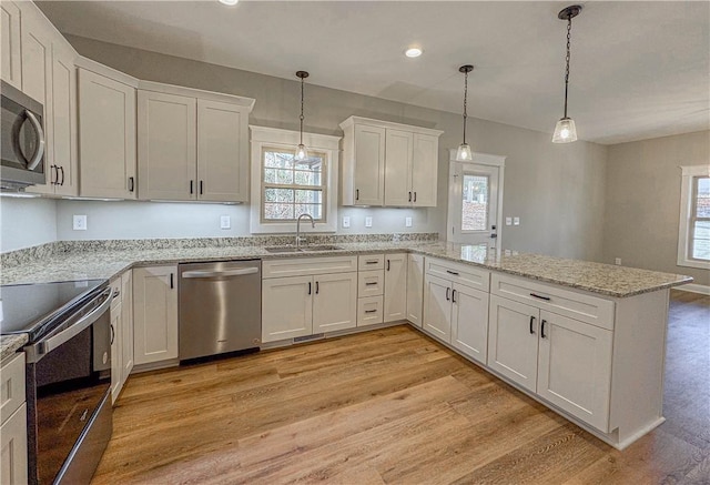 kitchen featuring stainless steel appliances, sink, light hardwood / wood-style flooring, white cabinetry, and hanging light fixtures