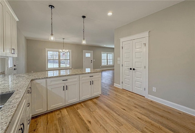 kitchen featuring light stone countertops, pendant lighting, light hardwood / wood-style flooring, a notable chandelier, and white cabinetry