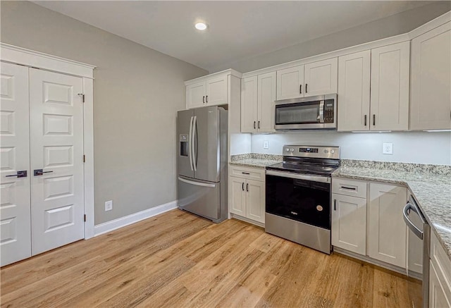 kitchen with white cabinets, light stone counters, light wood-type flooring, and stainless steel appliances