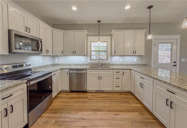 kitchen with hanging light fixtures, sink, white cabinets, and stainless steel appliances