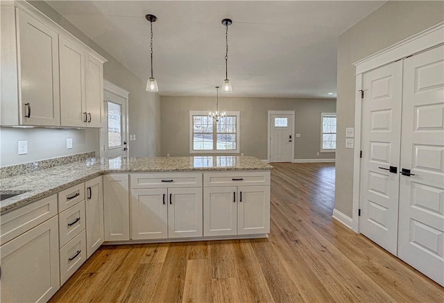 kitchen featuring decorative light fixtures, light hardwood / wood-style flooring, light stone countertops, a notable chandelier, and white cabinetry