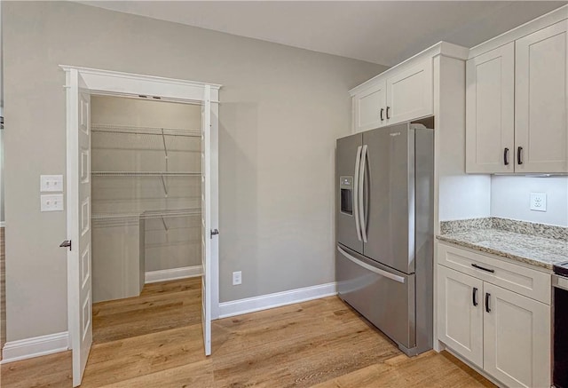 kitchen with light stone countertops, white cabinetry, light hardwood / wood-style floors, and stainless steel refrigerator with ice dispenser