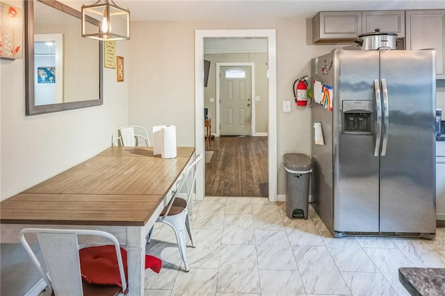 kitchen with stainless steel refrigerator with ice dispenser, light wood-type flooring, gray cabinets, and pendant lighting