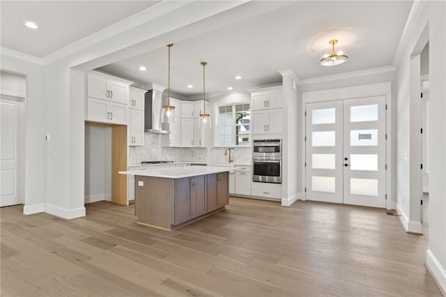 kitchen with white cabinetry, wall chimney exhaust hood, hanging light fixtures, light hardwood / wood-style flooring, and a kitchen island