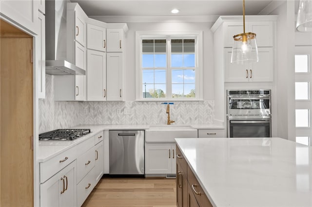 kitchen featuring decorative light fixtures, stainless steel appliances, white cabinetry, and wall chimney range hood