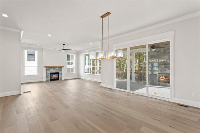 unfurnished living room featuring ceiling fan with notable chandelier, light hardwood / wood-style flooring, a stone fireplace, and ornamental molding