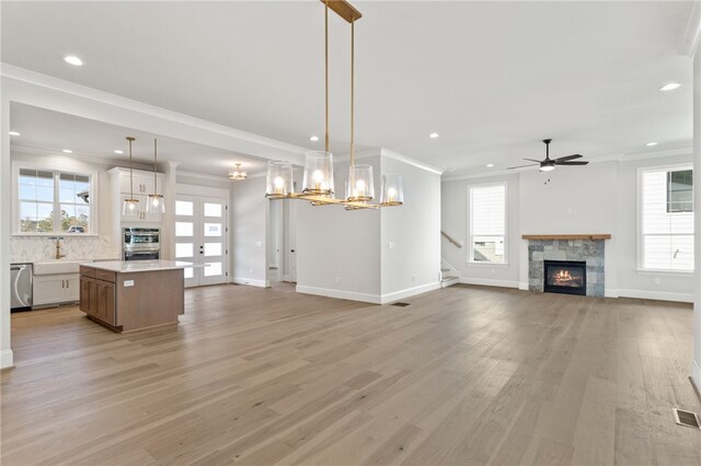 unfurnished living room featuring french doors, ceiling fan with notable chandelier, crown molding, light hardwood / wood-style flooring, and a fireplace