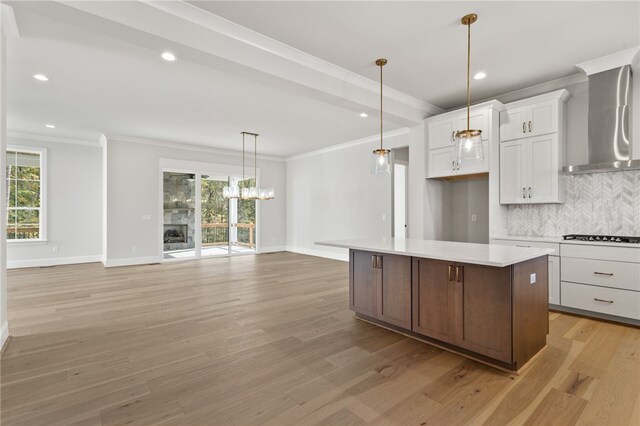 kitchen with white cabinets, light hardwood / wood-style flooring, a kitchen island, and wall chimney range hood