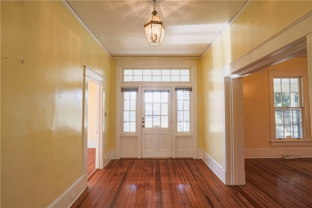 doorway with dark wood-style flooring, visible vents, crown molding, and baseboards