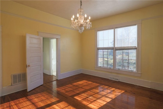 spare room featuring dark wood-style floors, visible vents, a notable chandelier, and baseboards