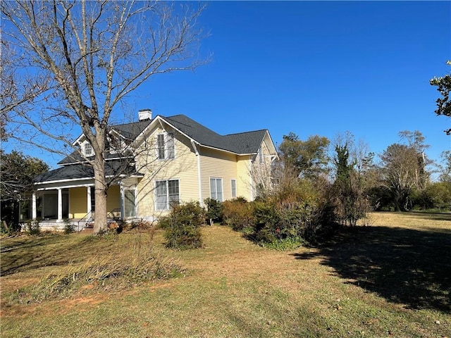 view of side of property with a chimney, a porch, and a lawn