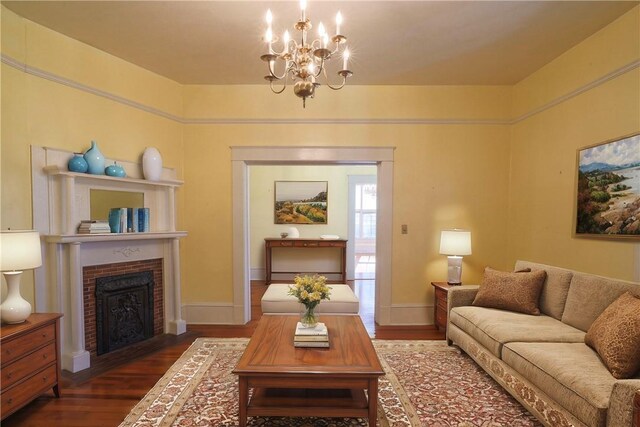 living area with a chandelier, dark wood-style flooring, a brick fireplace, and baseboards