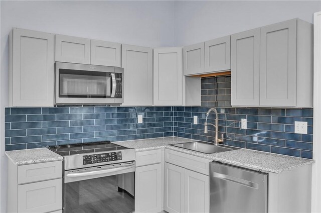 kitchen with stainless steel appliances, a sink, decorative backsplash, and light stone countertops