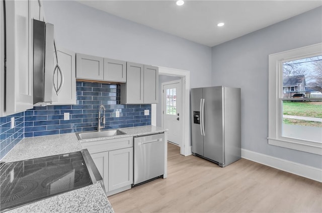 kitchen featuring stainless steel appliances, a sink, decorative backsplash, light stone countertops, and light wood finished floors