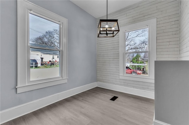 unfurnished dining area with a notable chandelier, wood walls, baseboards, and wood finished floors