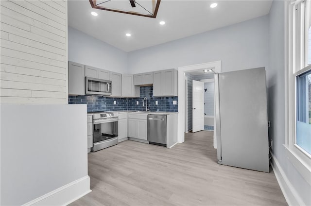 kitchen with stainless steel appliances, light countertops, gray cabinetry, decorative backsplash, and a sink