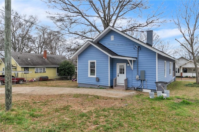 back of house with entry steps, a yard, a chimney, and dirt driveway