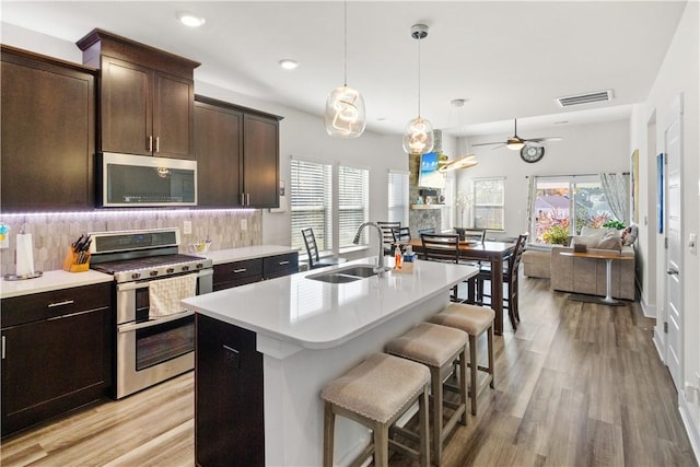 kitchen featuring ceiling fan, sink, stainless steel appliances, light hardwood / wood-style flooring, and an island with sink