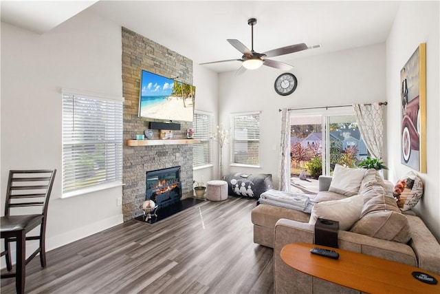 living room featuring a stone fireplace, a wealth of natural light, ceiling fan, and dark hardwood / wood-style floors