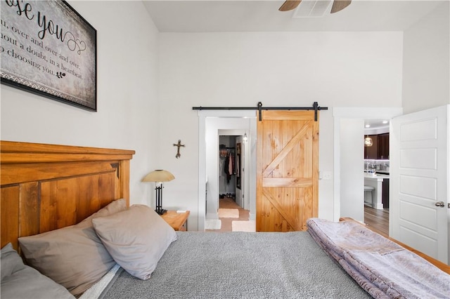 bedroom featuring hardwood / wood-style flooring, ceiling fan, a barn door, a spacious closet, and connected bathroom