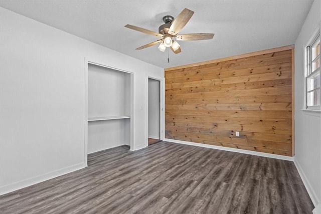 unfurnished bedroom featuring a closet, wooden walls, dark hardwood / wood-style flooring, and ceiling fan