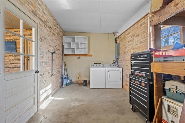 laundry area featuring washing machine and dryer, electric panel, and brick wall